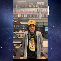 a young man in a hat is standing in front of a bookshelf