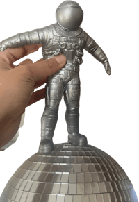 a person holding an astronaut figurine on top of a disco ball